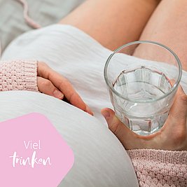 Schwangere Frau sitzend mit Wasserglas in der Hand